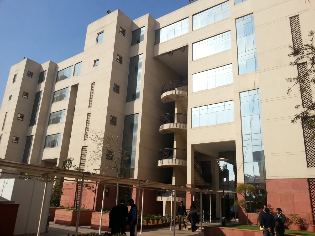 A tall cream-coloured block at NLU Delhi with curved balconies and glass windows, with a few people walking in the courtyard below
