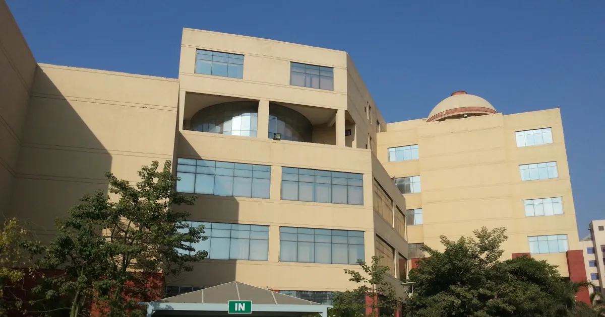 Cream-coloured main building of National Law University Delhi in Dwarka with a domed roof, green trees and a blue sky