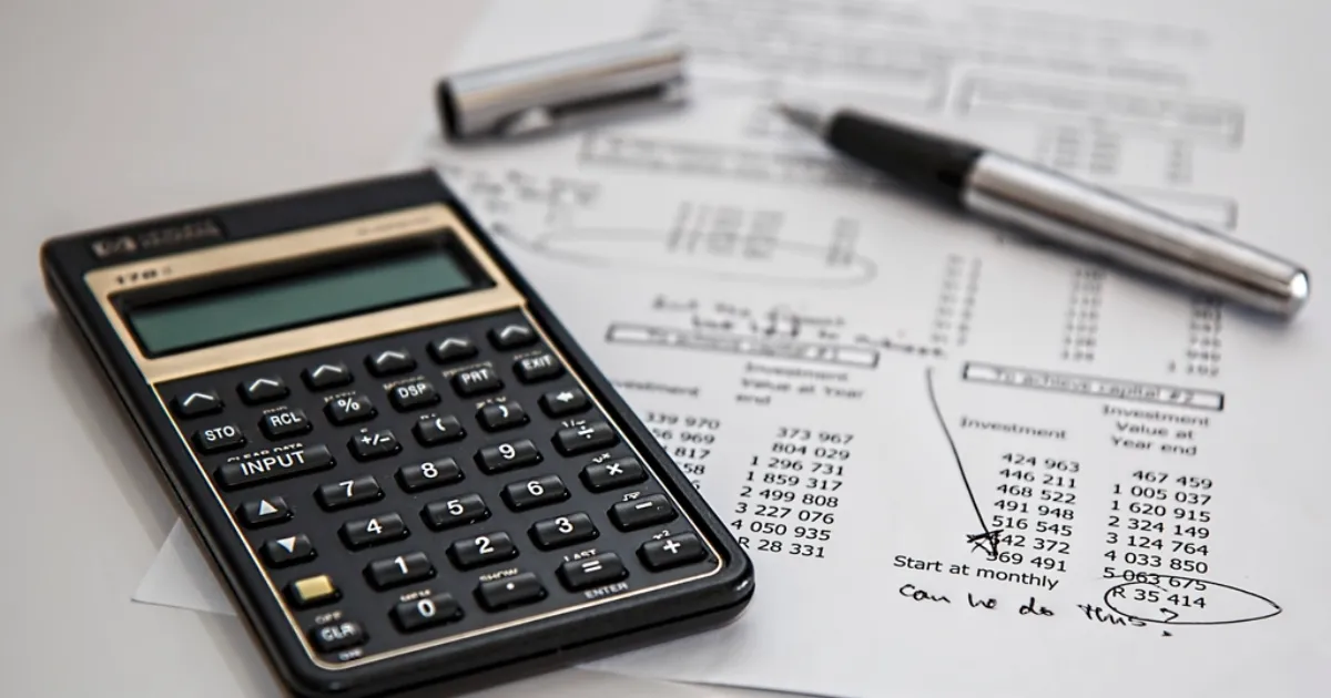 A black calculator and a silver pen lying on a printed sheet of figures with handwritten notes