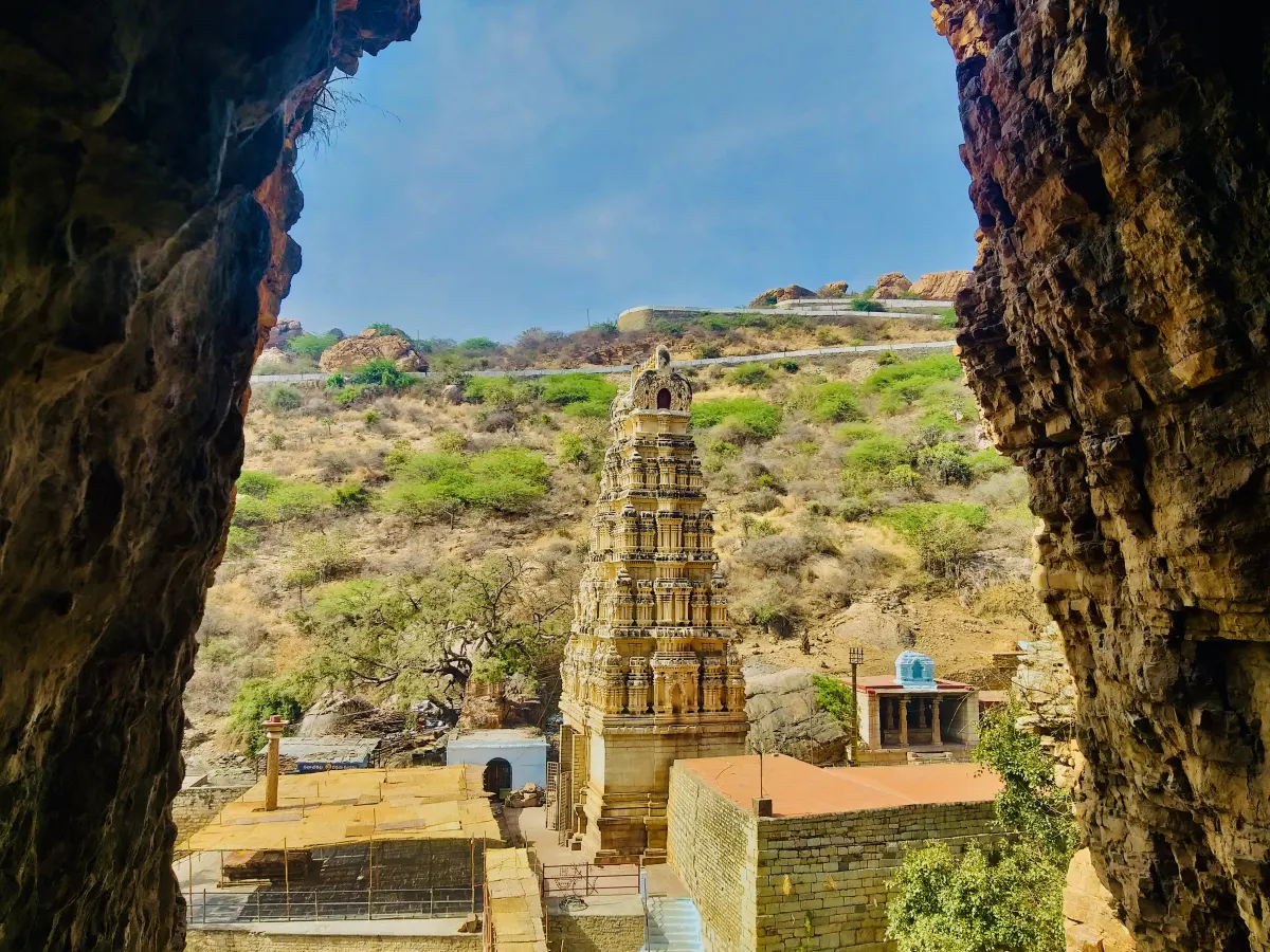 Looking out from a rock cave at the Yaganti temple tower in Kurnool district, with dry hills and scrub behind it