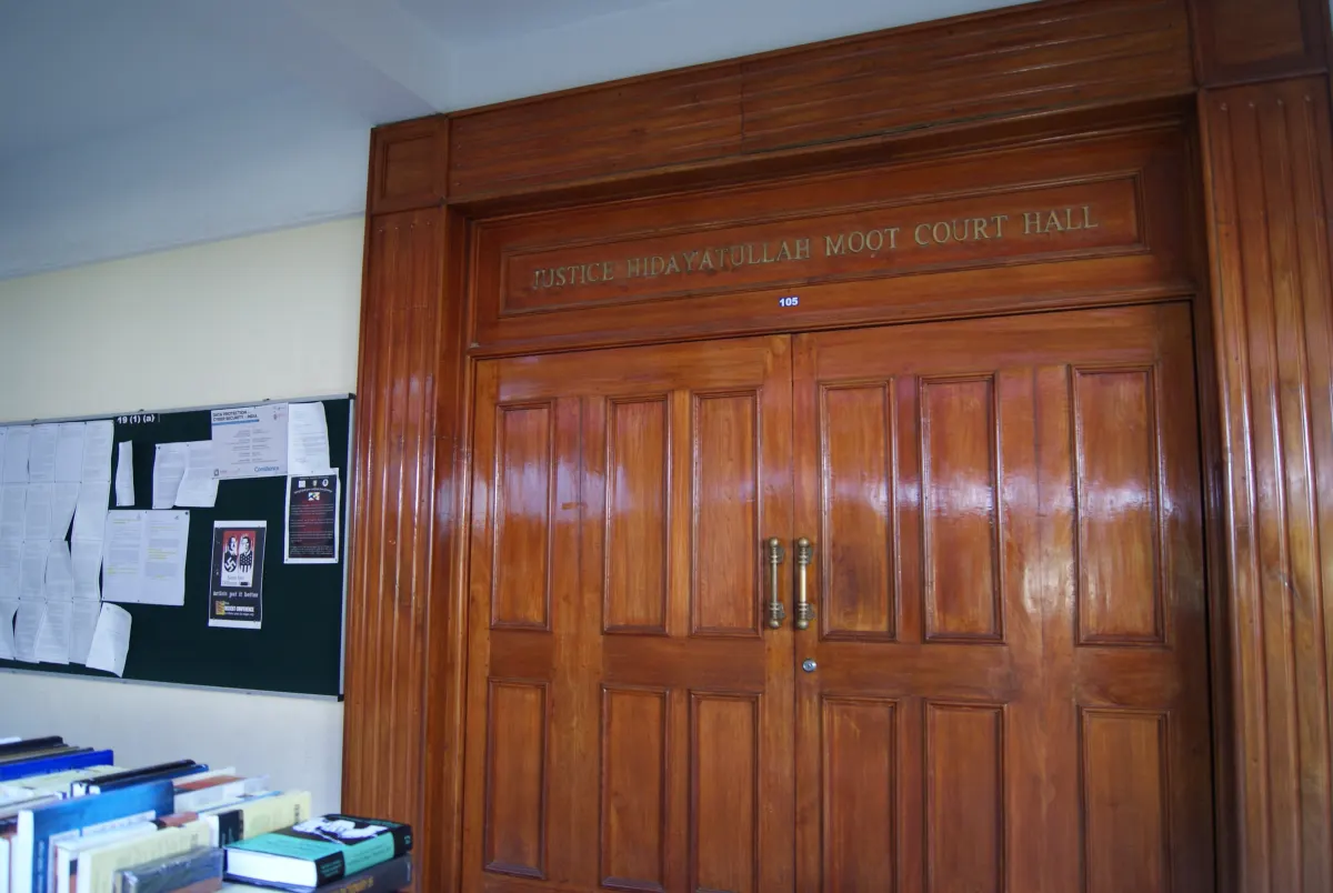 Wooden double doors of the Justice Hidayatullah Moot Court Hall at National Law School of India University, Bengaluru, with a notice board beside it