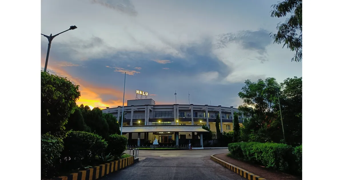 Main building of Hidayatullah National Law University, Raipur, at sunset, with a tree-lined road leading to it