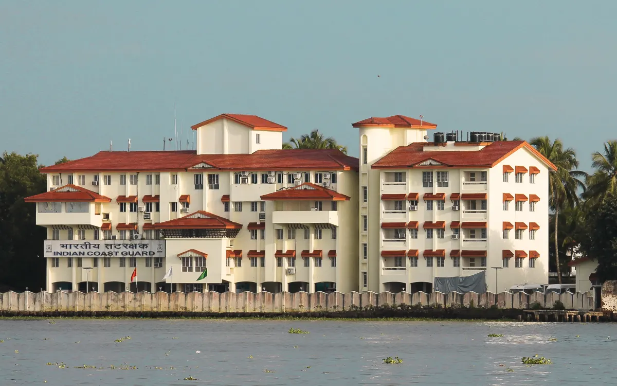 An Indian Coast Guard office building with white walls and red tiled roofs, seen from across the water