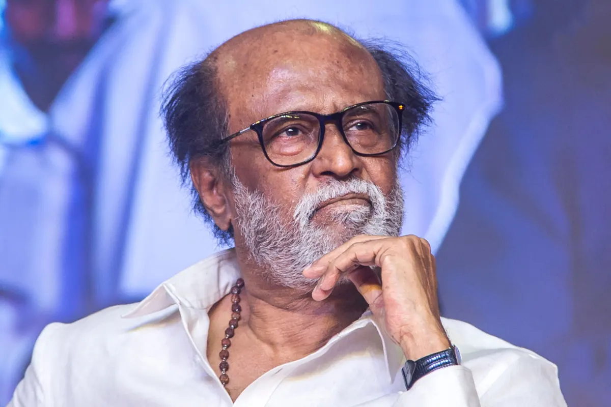 Rajinikanth in a white shirt and glasses at a public event, resting his chin on his hand