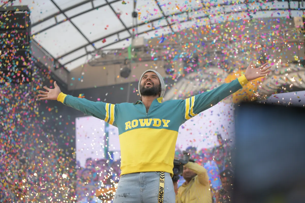 Vijay Deverakonda on stage with his arms spread wide as confetti falls around him at a fan event