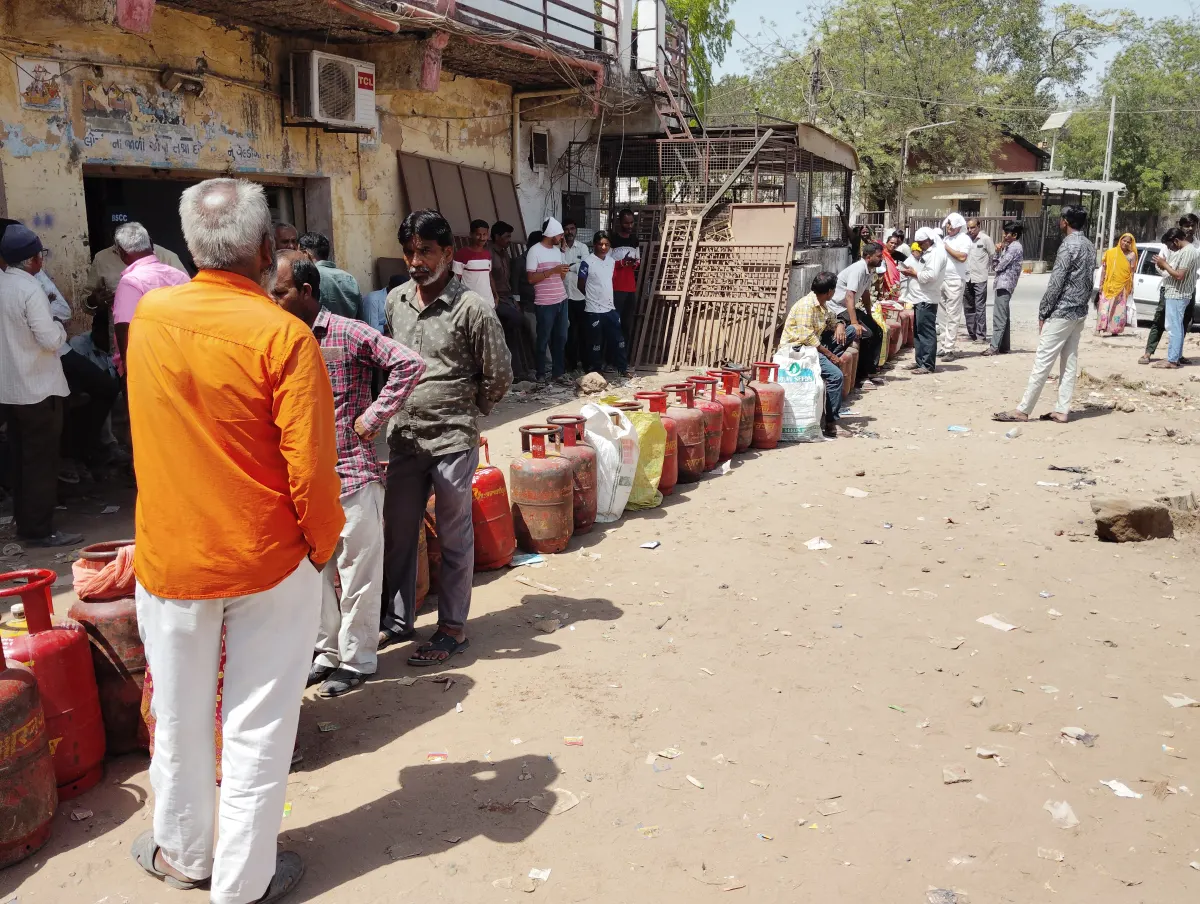 A queue of people with red LPG cylinders lined up on the ground outside a gas distributor