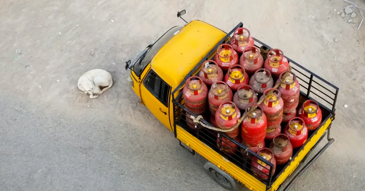 A yellow goods carrier loaded with red LPG cylinders, seen from above on a street in Hyderabad