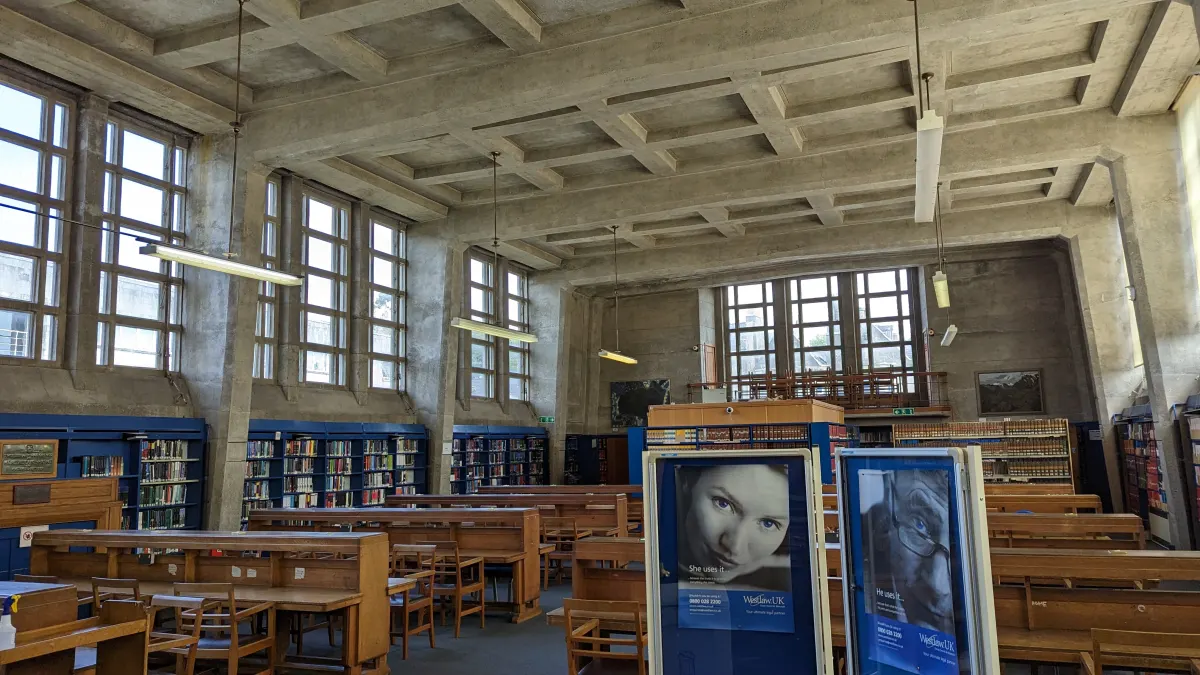 A long, quiet library reading room with rows of wooden desks and bookshelves