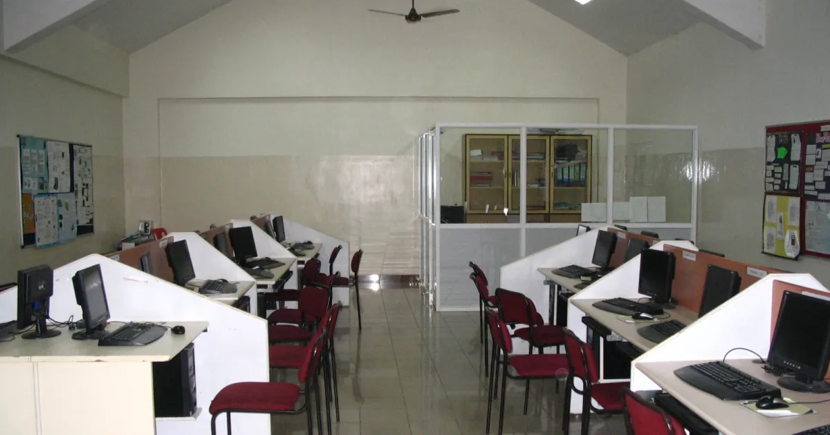 An empty computer lab with rows of desktop computers on white desks and red chairs