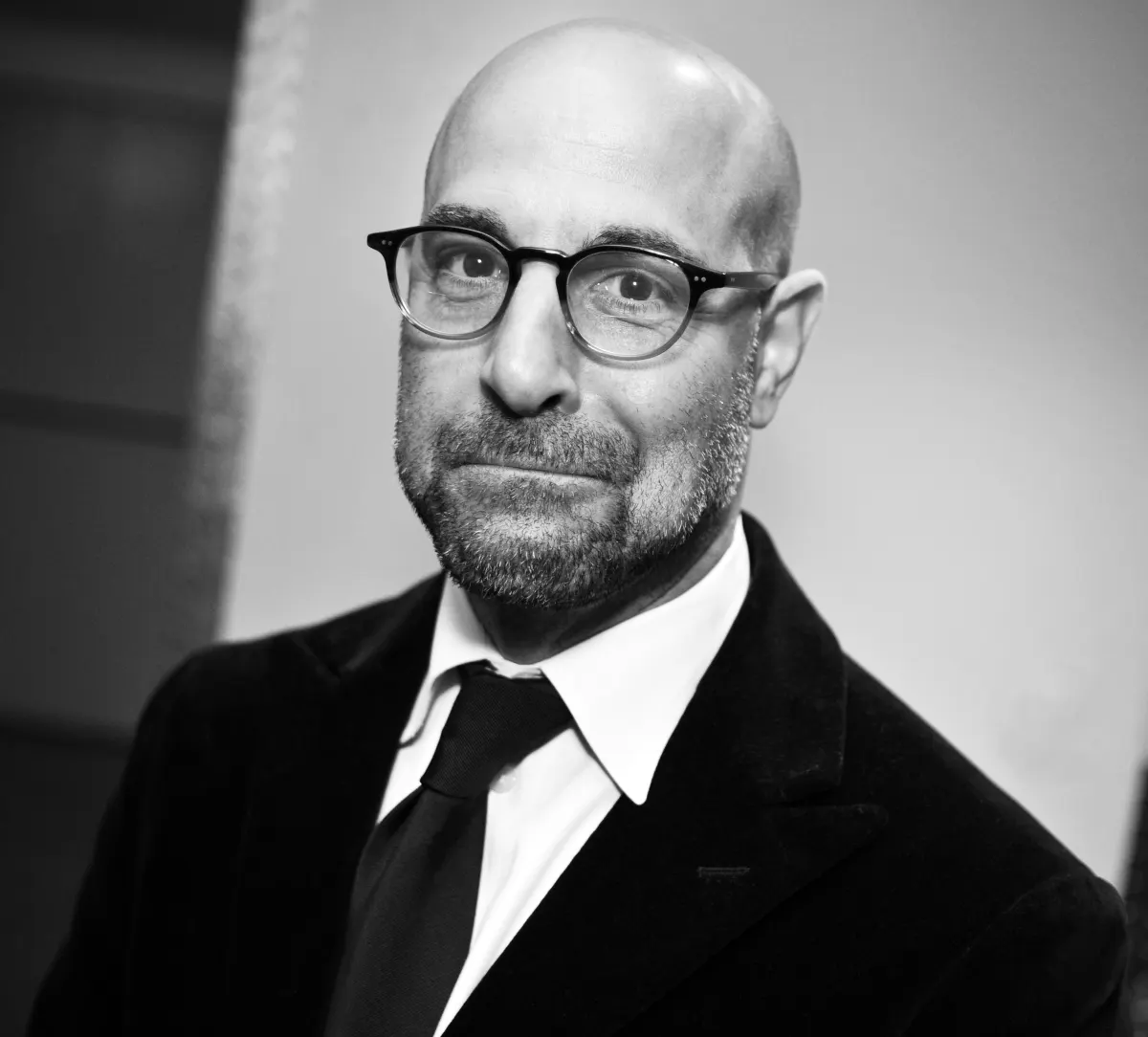 Black and white portrait of actor Stanley Tucci in glasses, a dark suit and tie