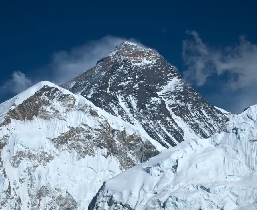 The snow-covered peak of Mount Everest under a blue sky with clouds