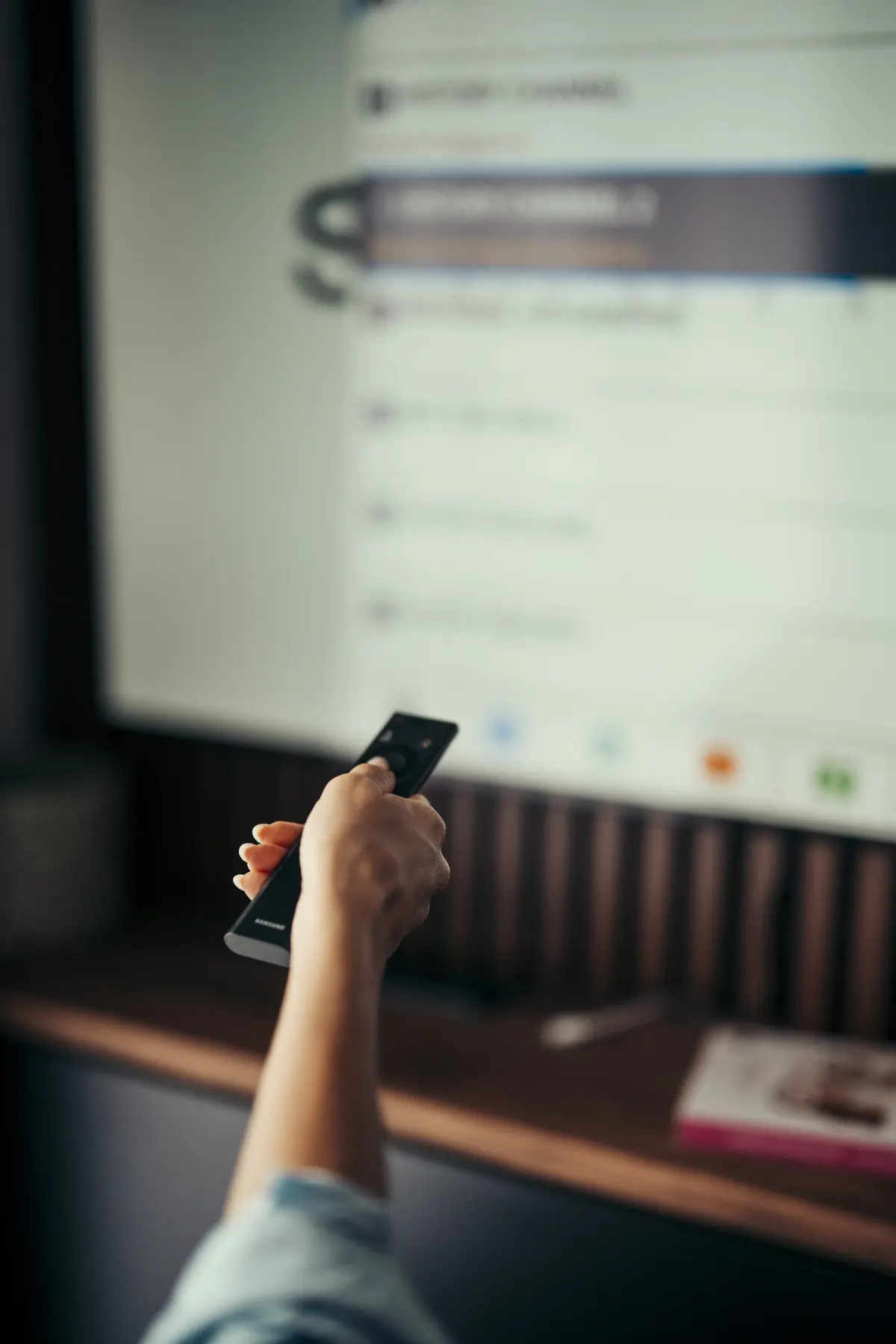 A hand pointing a remote control at a large TV screen showing a menu in a living room