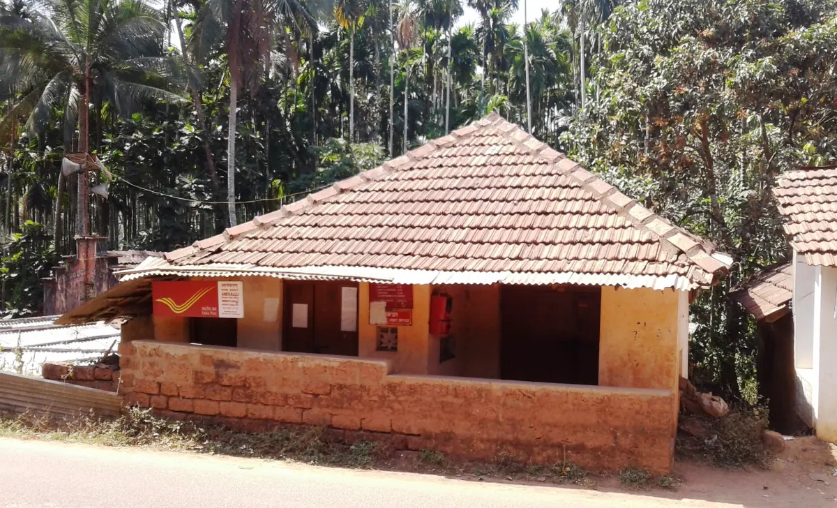 A small village post office with a tiled roof and red India Post signboards beside a road