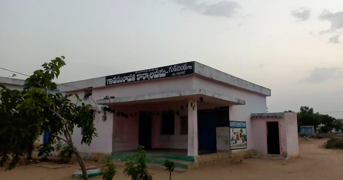 A single-storey gram panchayat office in a Telangana village, with a blue tractor, a water tanker and motorcycles parked in front