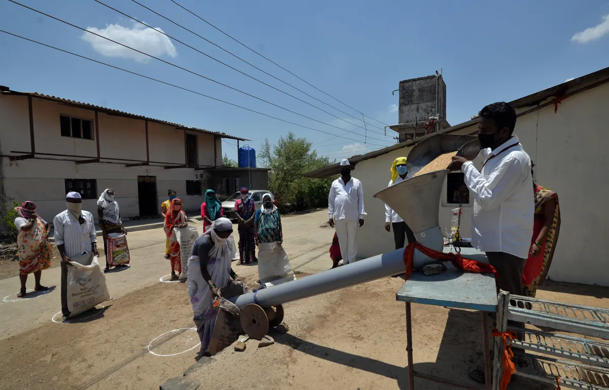 People standing in marked circles in an open yard while workers hand out ration grain from sacks