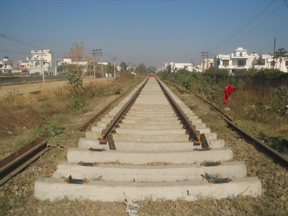 A newly laid railway track on concrete sleepers stretching into the distance, with fresh ballast and houses on both sides