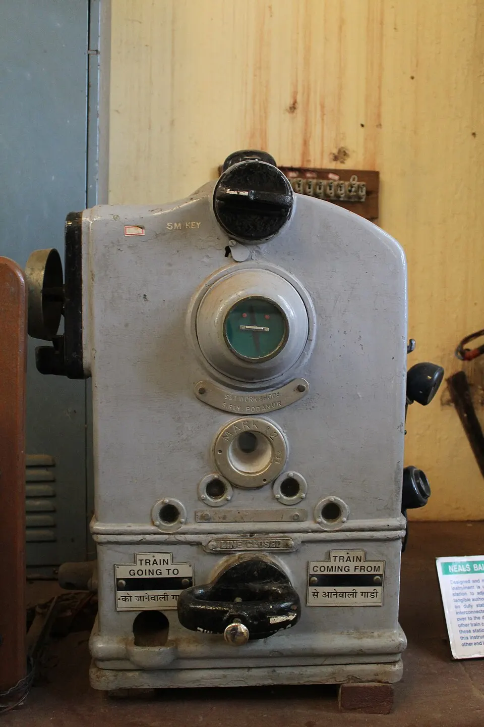 A grey Neale’s ball token instrument with an SM key slot and labels for trains going to and coming from the next station