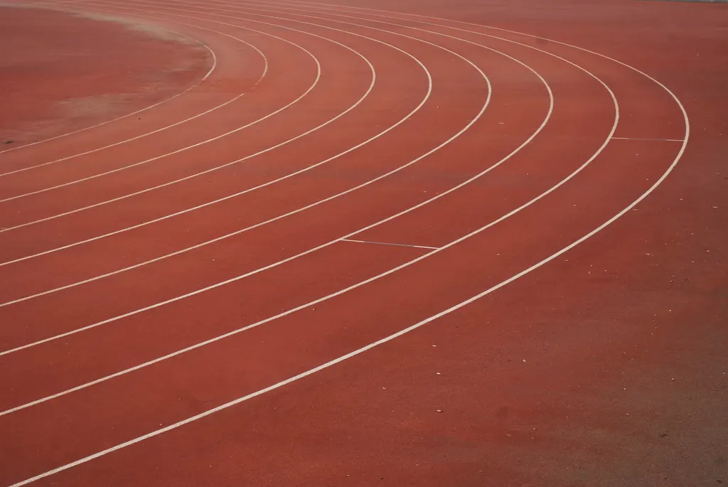 An empty red running track with white lane lines on a curve