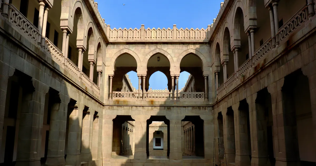The stone inner courtyard of Osmania University Arts College in Hyderabad, with rows of arches under a blue sky