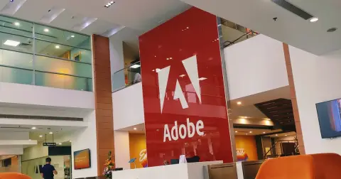 The red Adobe wall with the white Adobe logo in the lobby of Adobe's office in Noida, with orange chairs in front