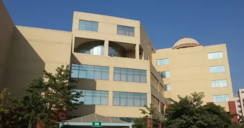 Cream-coloured main building of National Law University Delhi in Dwarka with a domed roof, green trees and a blue sky