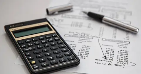 A black calculator and a silver pen lying on a printed sheet of figures with handwritten notes