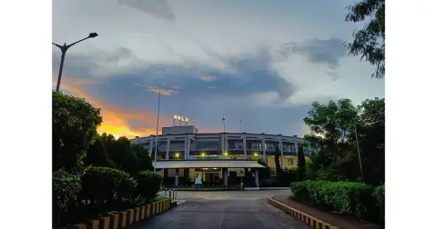 Main building of Hidayatullah National Law University, Raipur, at sunset, with a tree-lined road leading to it