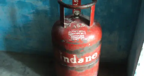 A red Indane 14.2 kg domestic LPG cylinder standing in a corner against a blue wall
