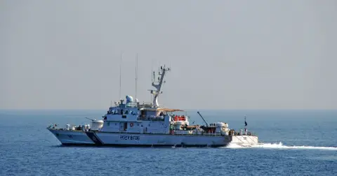 A white Indian Coast Guard patrol ship with a blue and orange stripe sailing on calm blue sea