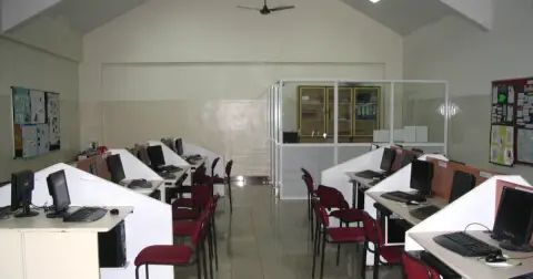 An empty computer lab with rows of desktop computers on white desks and red chairs