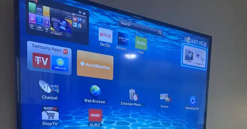 A wall-mounted smart TV showing its home screen with app tiles on a blue background