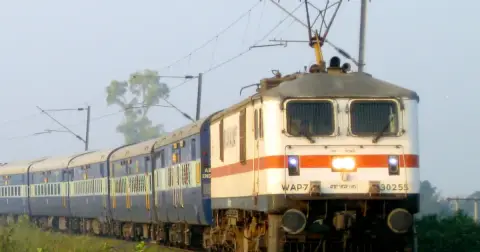 A WAP-7 electric locomotive of Indian Railways pulling a blue passenger train on a curve under overhead wires